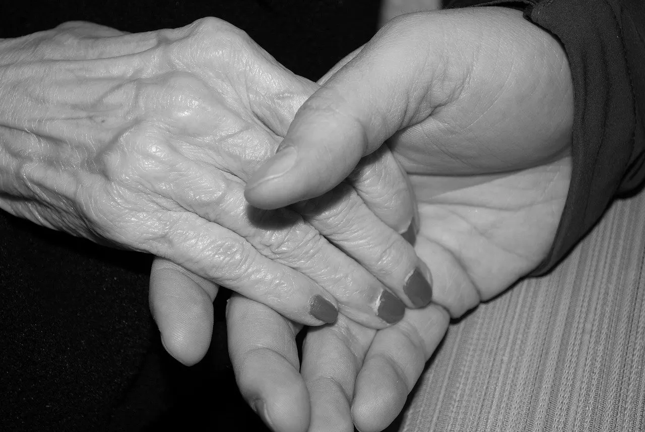 Schwarzweißfoto: Eine faltige alte Hand mit lackierten Nägeln liegt in einer jüngeren Hand, die sie von unten hält